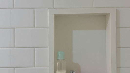 Niche aménagée dans un mur carrelé blanc de salle de bain, avec un petit flacon